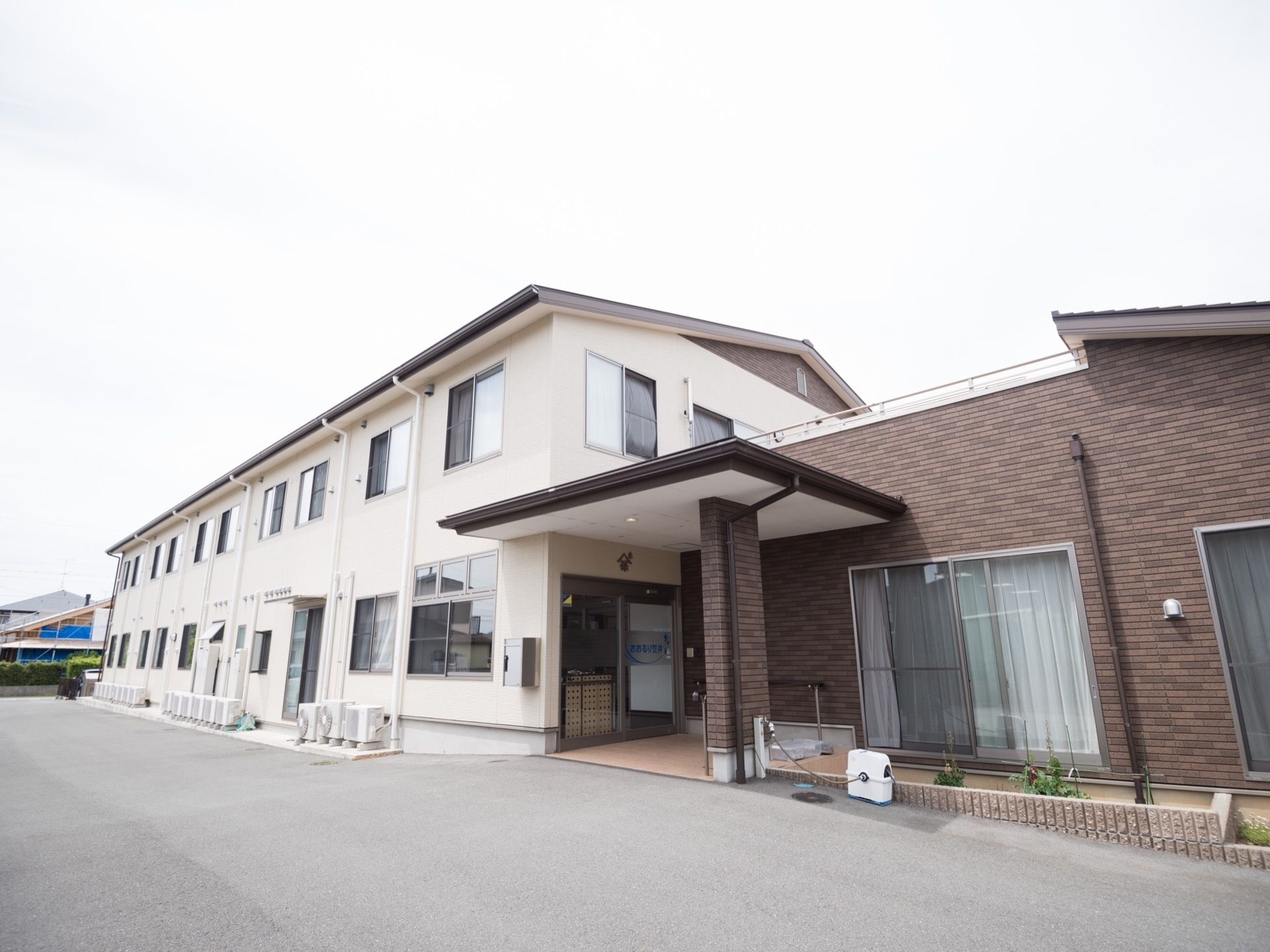 2階建ての白い建物で、玄関には大きなひさしが設置されている。建物に沿ってレンガ造りの花壇が置かれている。