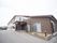 2階建ての白い外壁の建物と屋上のある1階建ての茶色の建物が繋がって建てられている。施設前の路面は舗装されている。