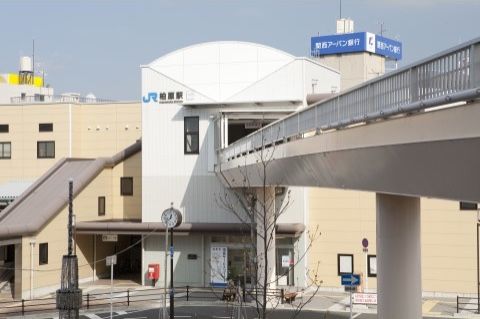 最寄り駅の外観である。駅前を通る道路の上に架けられた陸橋があり、2階の改札階へと続いている。駅前には郵便ポストがある。