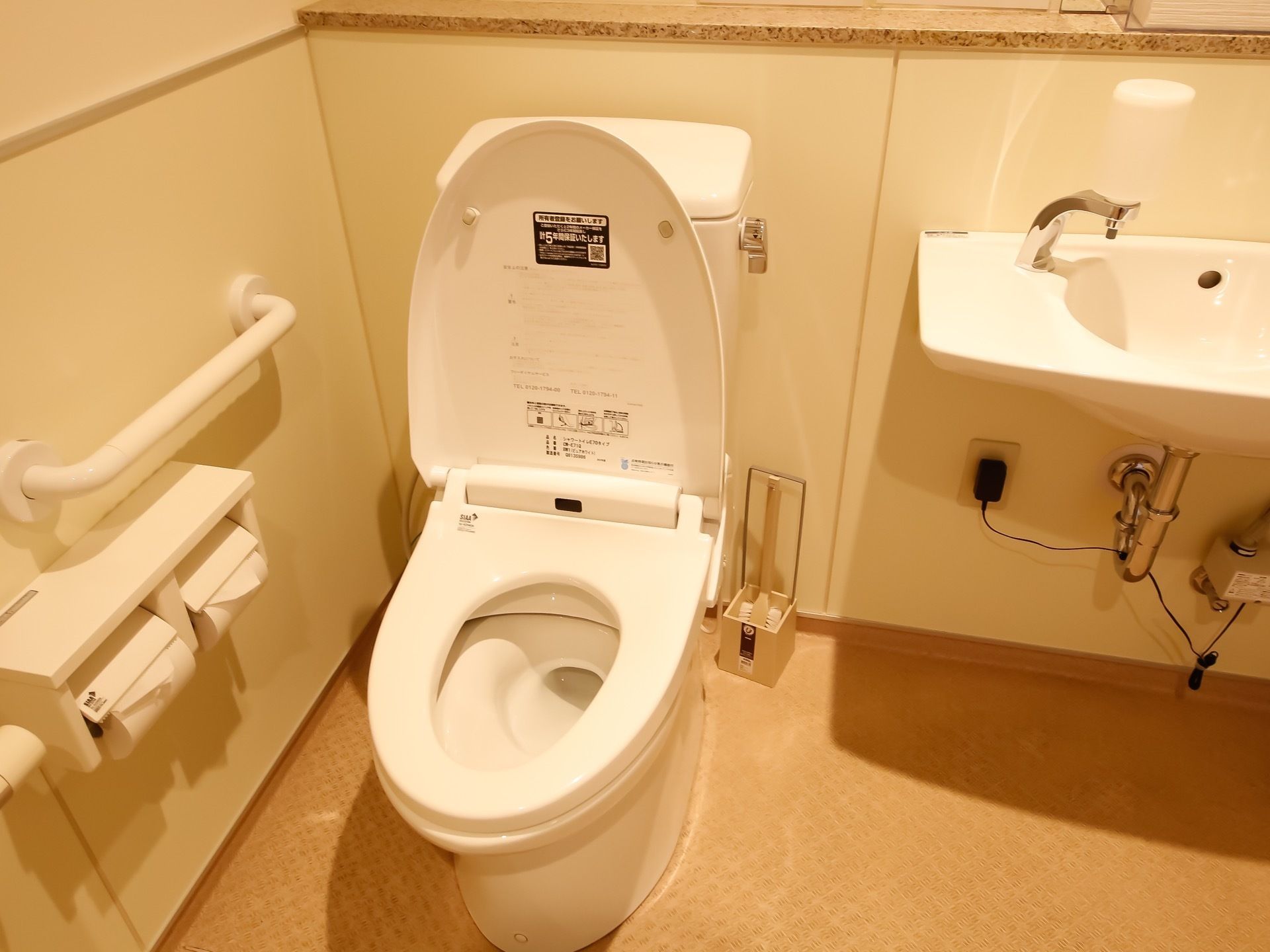 洗面台を備えたトイレスペースである。便座横の壁に手すり、トイレットペーパーホルダーを２ヶ所設置している。