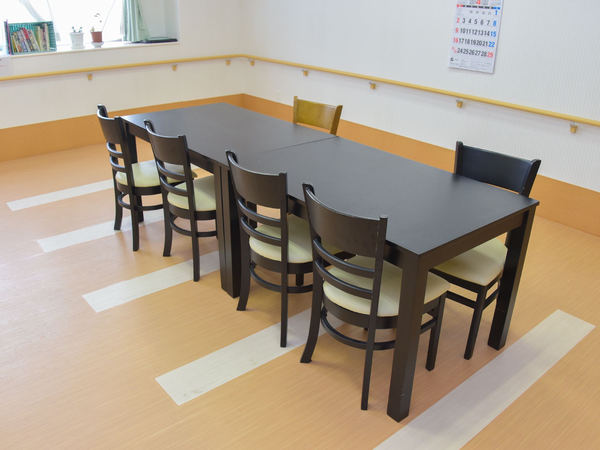 茶系のテーブルとイスが置かれた落ち着いた雰囲気の談話室。利用者同士の交流だけでなく、窓側に置かれた本を読むなど、様々な活用ができる。