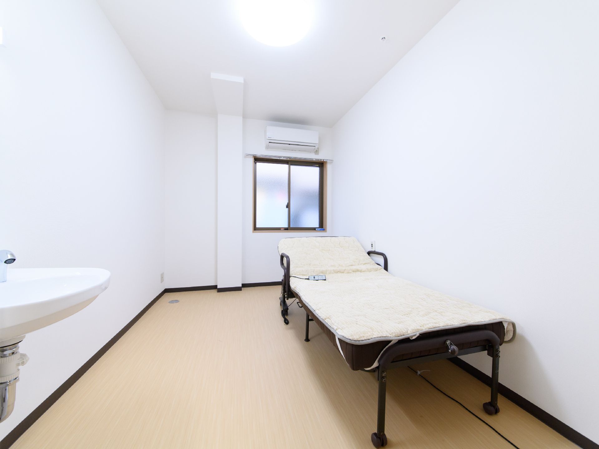 居室には、介護ベッド、洗面台、エアコンが設置されている。窓があるが、すりガラスになっているため中の様子がわかりにくい。