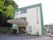 三階建て、明るいベージュ色と緑色に縁どられた建物。。出入り口には雨除けがある。多数の植木鉢が施設を彩る。