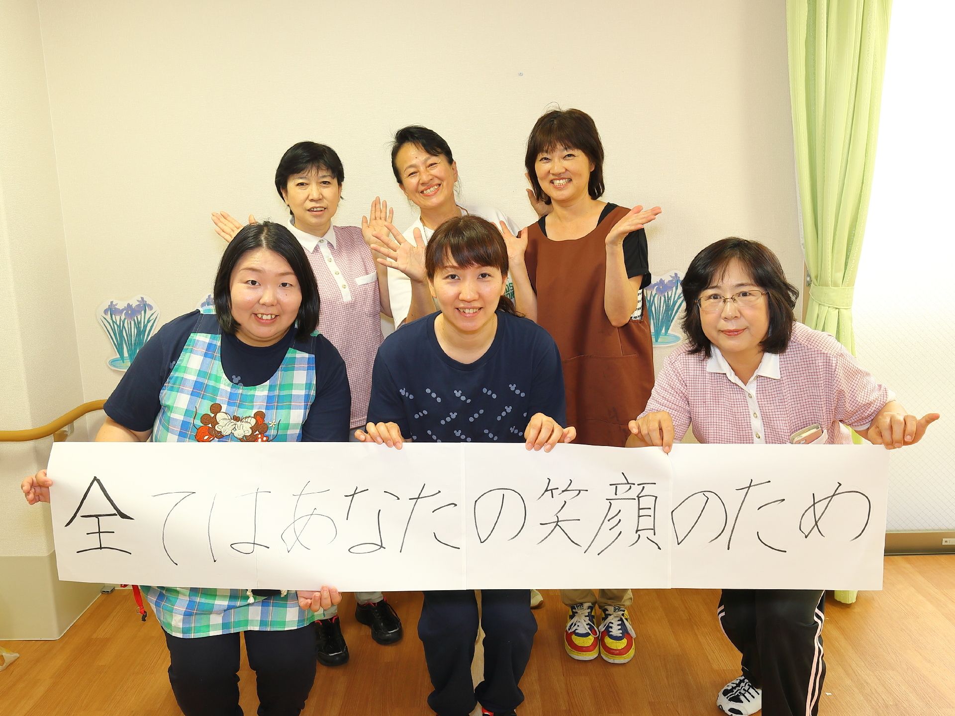 明るく、楽しそうな雰囲気の女性スタッフたちが写っている。モットーの横断幕を掲げ、介護への意欲を表している。