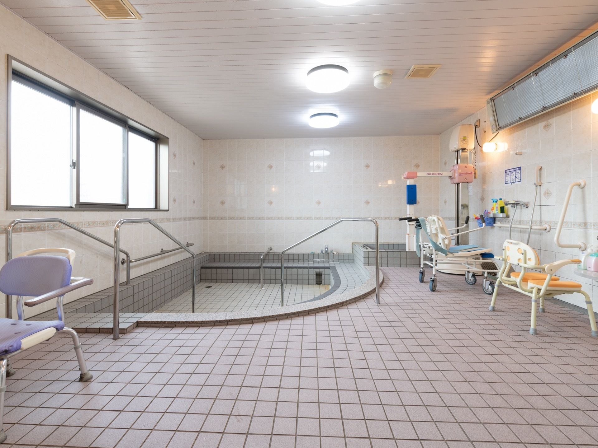 大きな浴室に掘り込み式の浴槽があり、出入りのための手すりがある。洗い場には手すりが設置されている。背もたれのある椅子も置いてある。