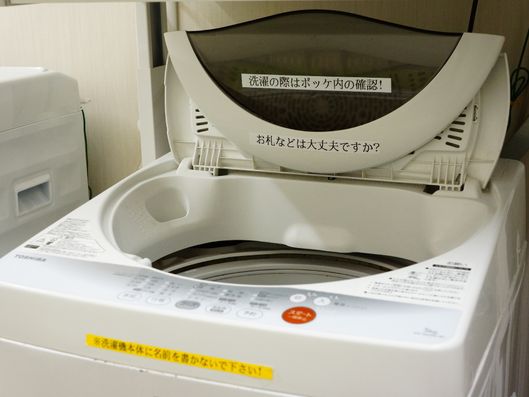 洗濯機には、洗濯物を入れる前にうっかりお金などを洗ってしまわないように注意喚起する貼り紙がついている。