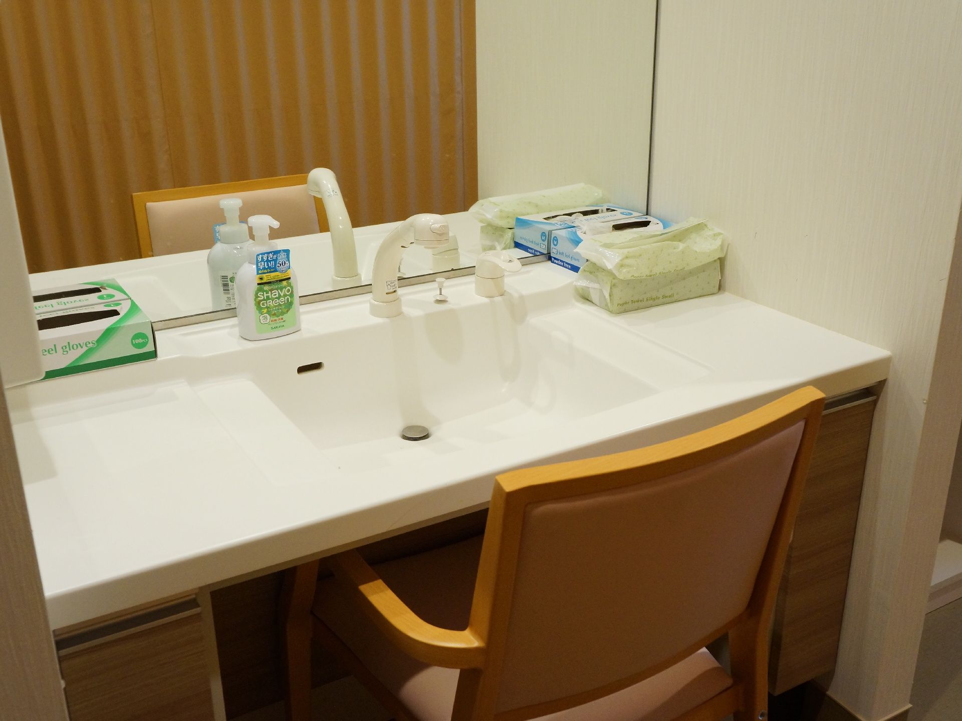 脱衣場の洗面台は木目調と白のデスク状になっていて白の蛇口があり石鹸やタオルなどの備品も置かれている。サイズの合う椅子も置かれている。
