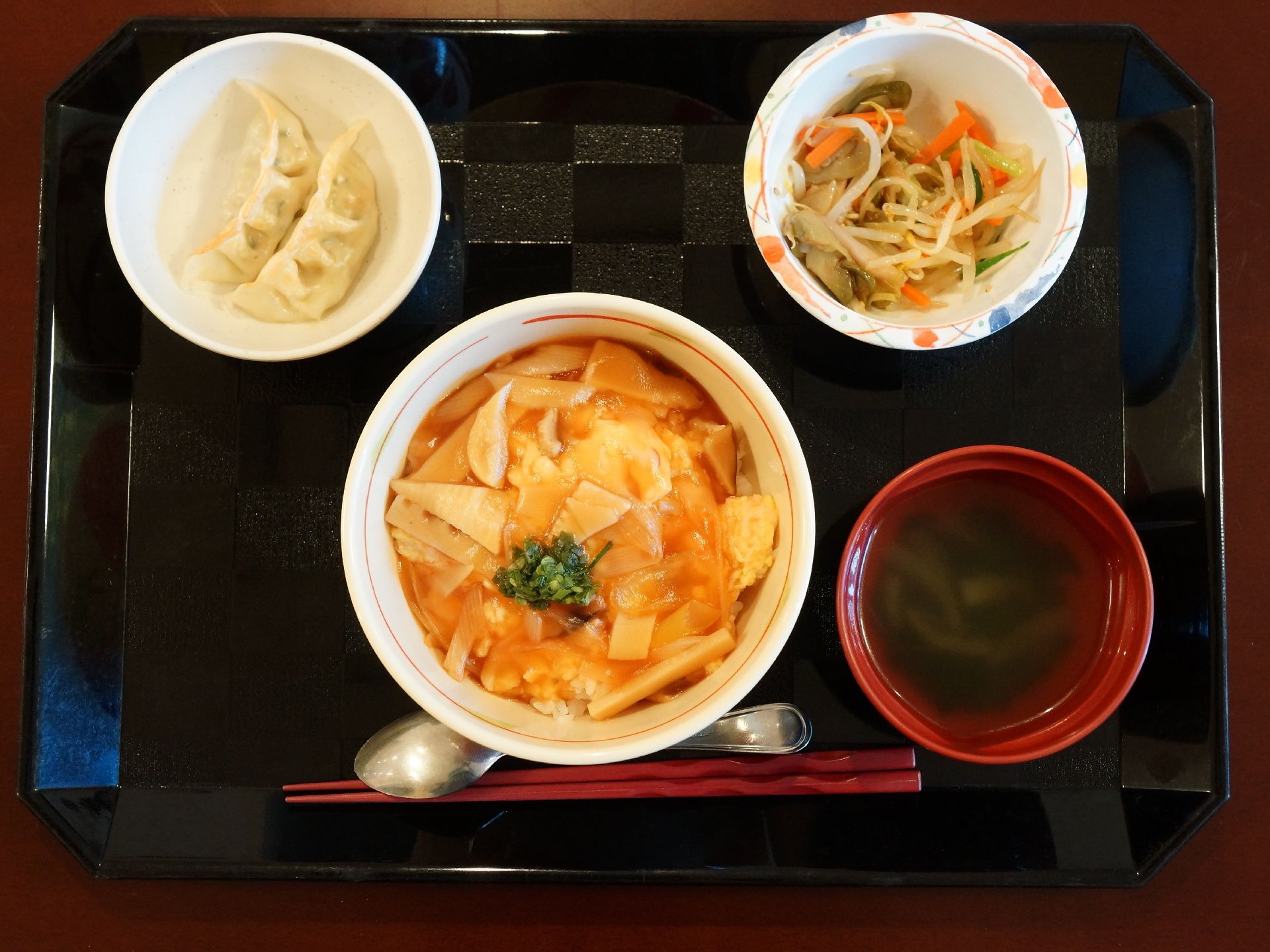 黒いデザインのお盆の上には、4種類の食事がのっており、主菜と副菜がバランス良く取られている。また、箸とスプーンが添えられている。