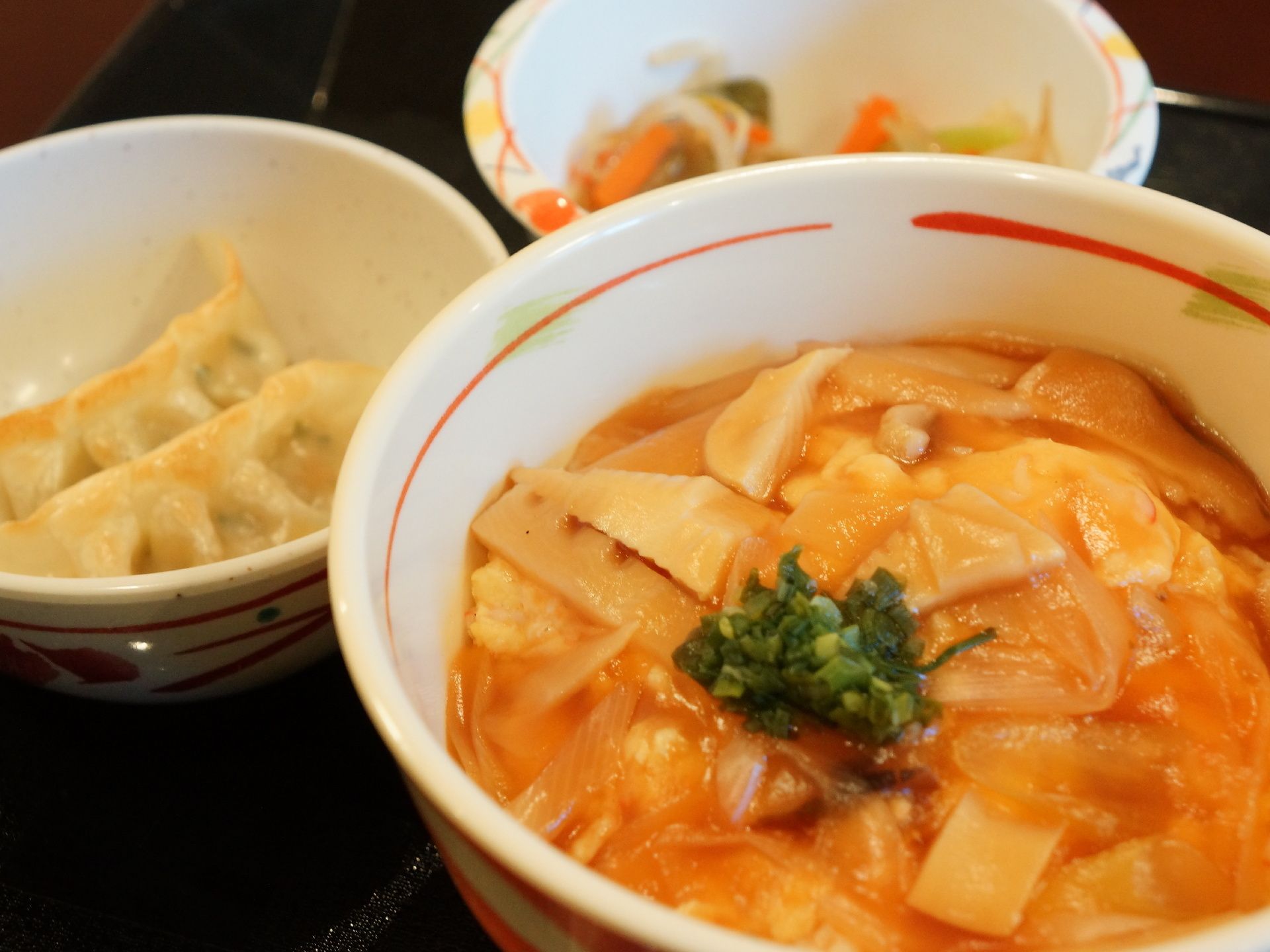 お盆の上には食事があり、様々な具材がのっている丼ぶりもの、餃子、もやしの炒め物のいったものを確認することができる。