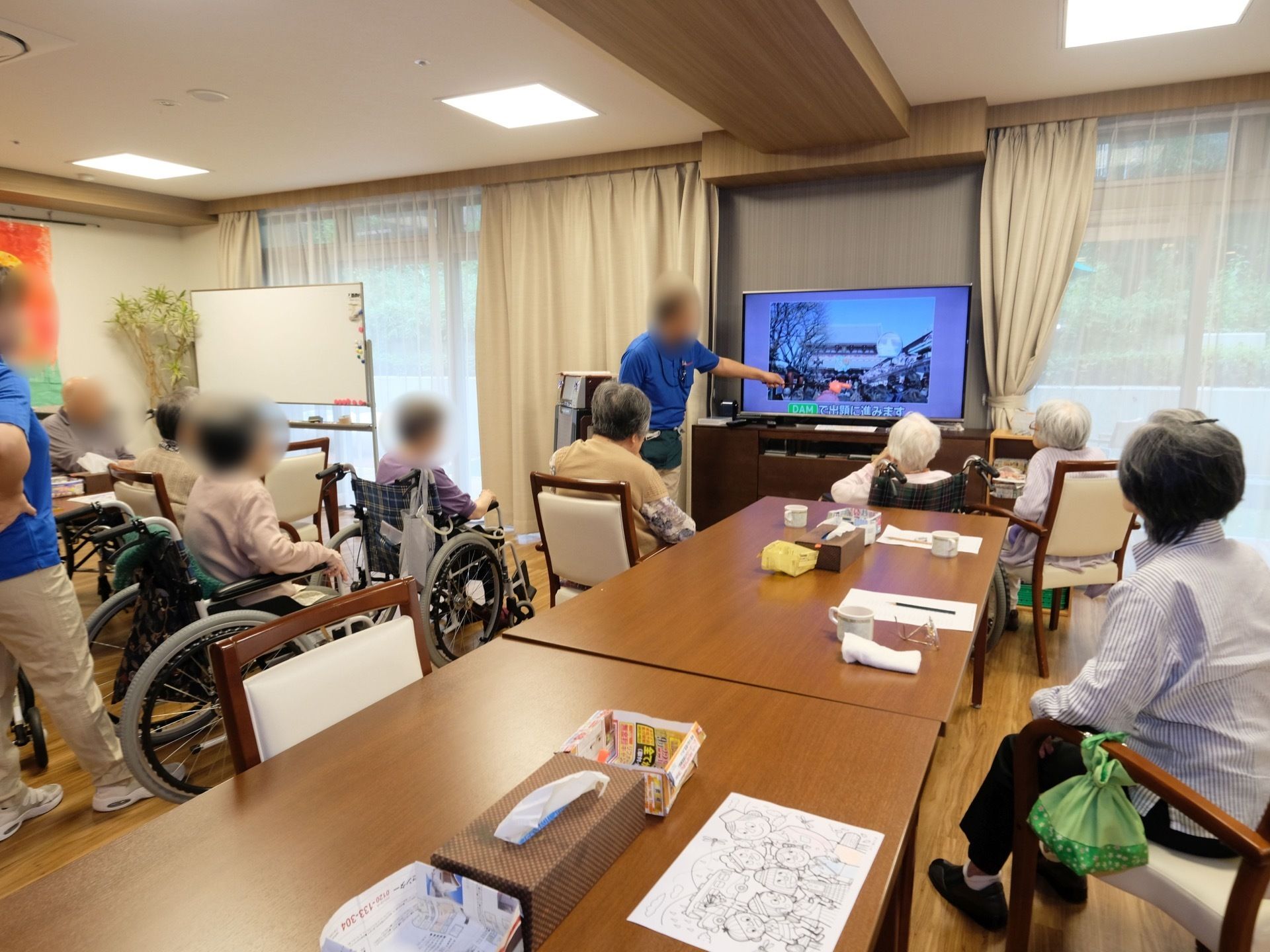 これは、食堂でモニターに映し出されているものをスタッフが入居者様に説明している様子。スタッフは常駐しているので安心して過ごせる。