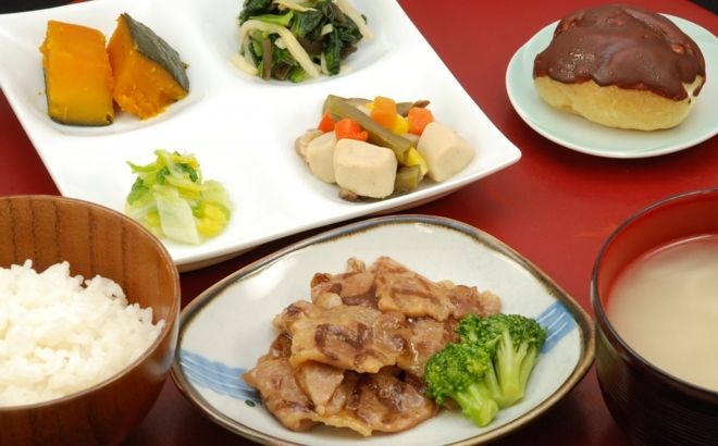 肉の炒め物やかぼちゃの煮物、ほうれん草のおひたし、エクレアのデザートが付いたメニュー