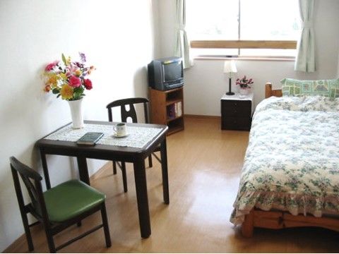 テーブルと小棚の上に花が飾ってあるテレビ付きの個室