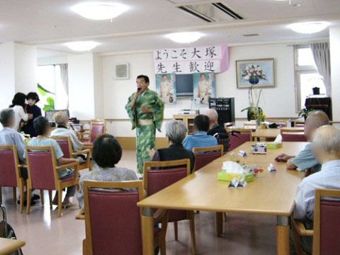 前で着物を着てマイクで歌う男性と椅子に座っている入居者