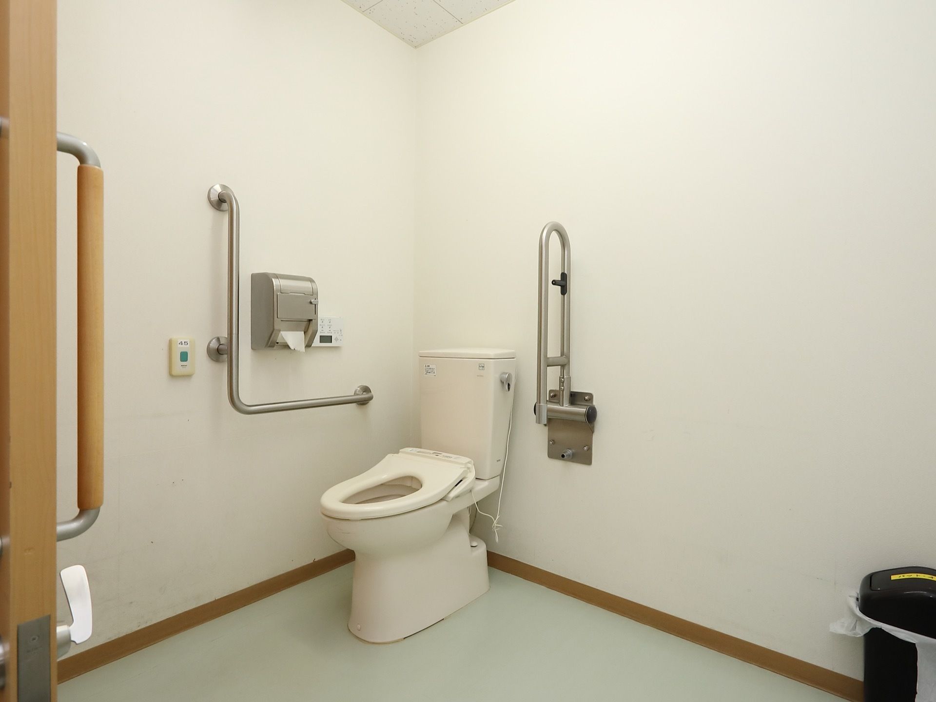 車椅子でも余裕を持って入れる洋式トイレがある。扉は引き戸で、便座の近くには金属の手すりが設置されている。