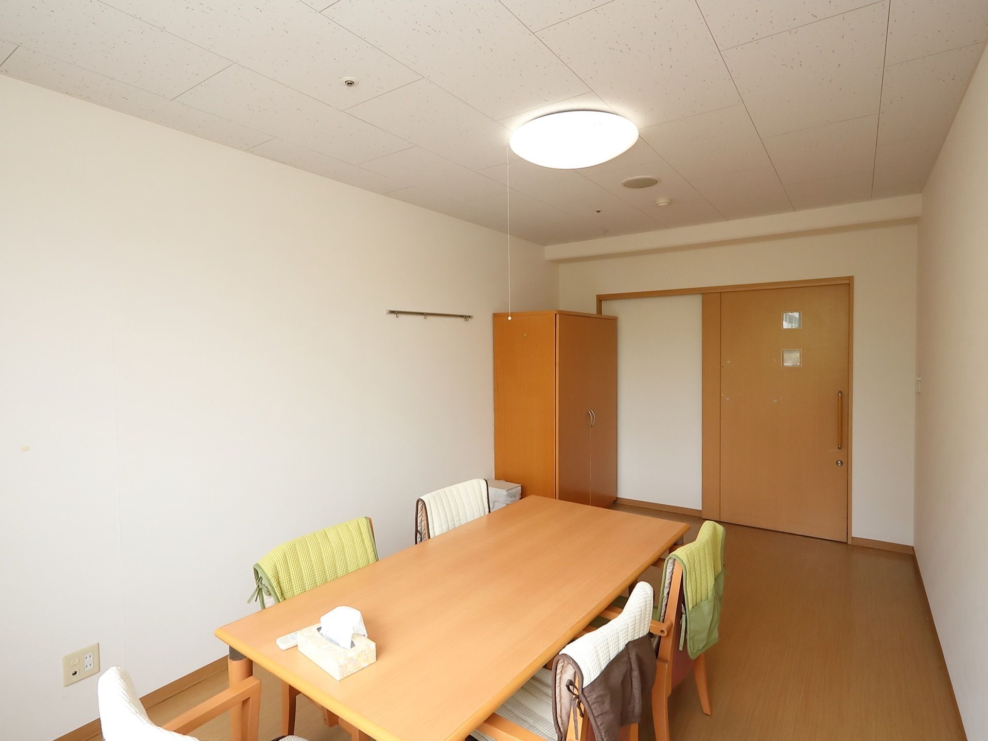 引き戸を入ると右手に木製のクローゼットがある。部屋の中央にはダイニングテーブルがあり、椅子が5脚置かれている。