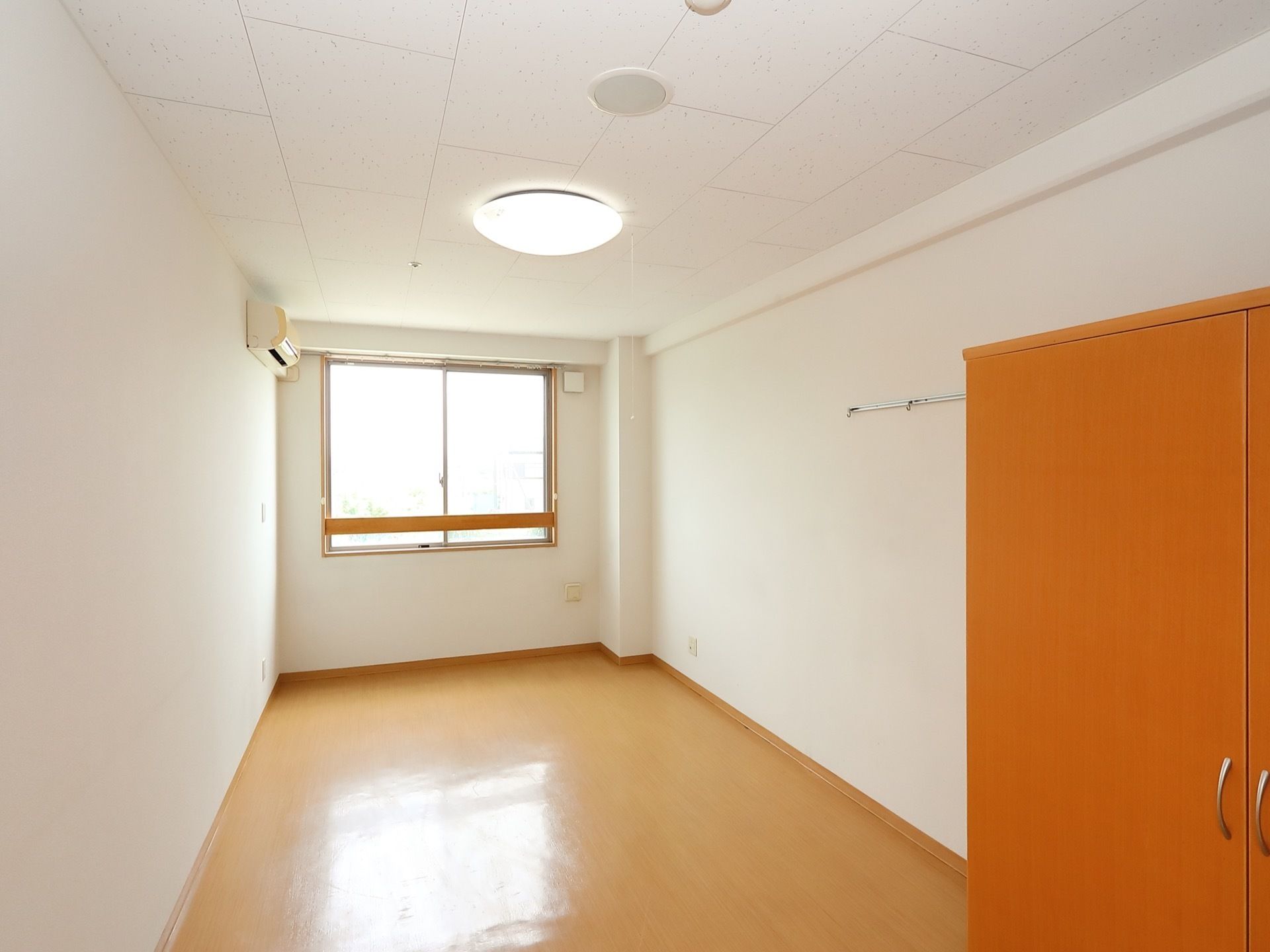 収納棚が置かれたフローリングのシンプルな部屋がある。突き当りの壁には窓がついていて、自然光も良く入っている。
