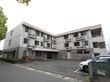 白とグレーの2色が印象的な3階建てのマンションが建っている。敷地内は舗装されていて、駐輪場や駐車場が整備されている。