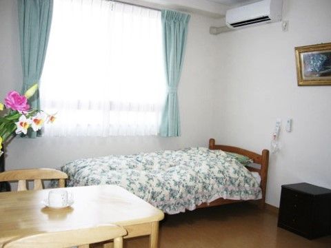居室の奥にある、かわいらしい花柄のベッドカバーがかけられた木製ベッド