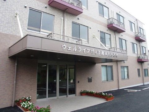 エントランス両脇に植木鉢の花が並ぶ、3階建ての施設
