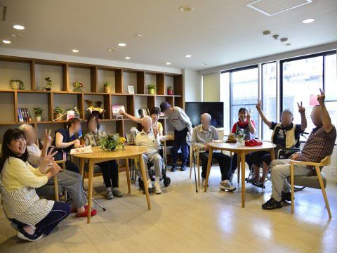 丸いテーブルを囲み、ピースサインで手をあげ楽しむ入居者とスタッフ