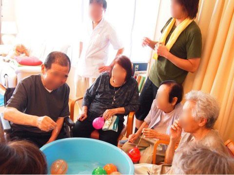 椅子に腰かけながら水風船釣りを楽しむ入居者と見守るスタッフ