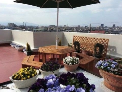 パラソル付きのガーデンテーブルセットが設置され、色とりどりのお花が植えられた鉢やプランターが置かれた屋上
