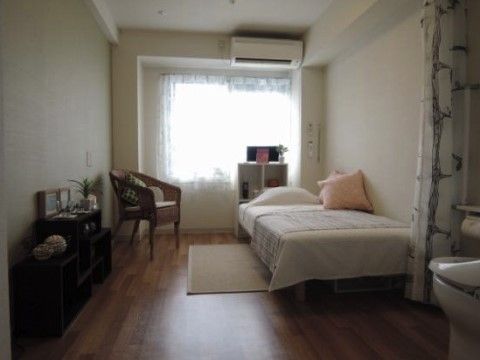 ベッド、棚、椅子、エアコン、トイレが備えられた明るい居室