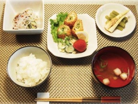 ランチョンマットに乗せられた、ご飯、お吸い物、メイン料理、小鉢、小皿とお箸