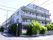 施設は4階建てのタイルの外壁の白いマンション風の建物。塀の周囲には木が植えられている。通りに面していて看板も設置されている。