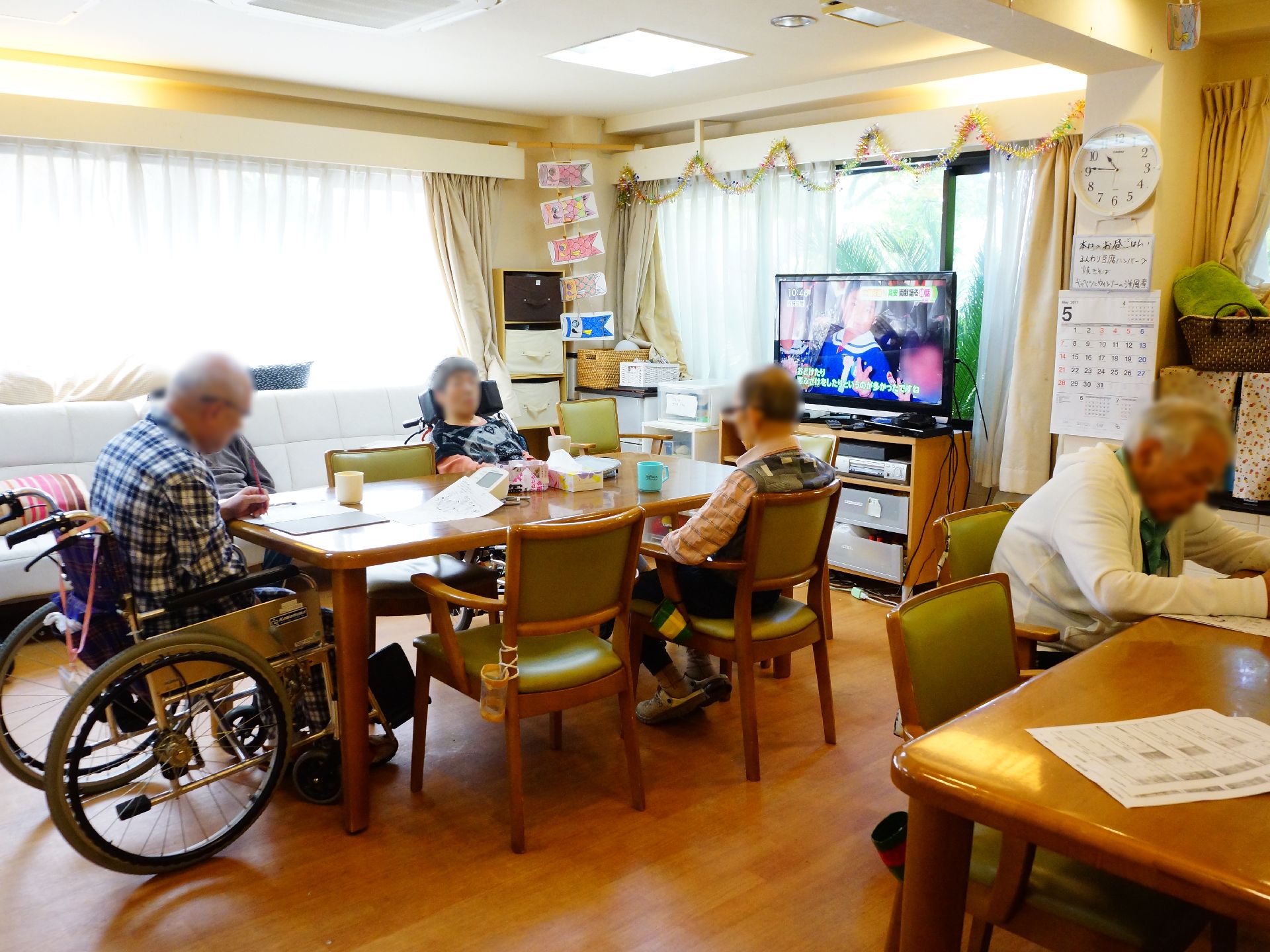 リビングの窓際には大人数が座ることができる白井ソファーも設置されている。また車椅子のままテーブルを利用している入居者も写っている。