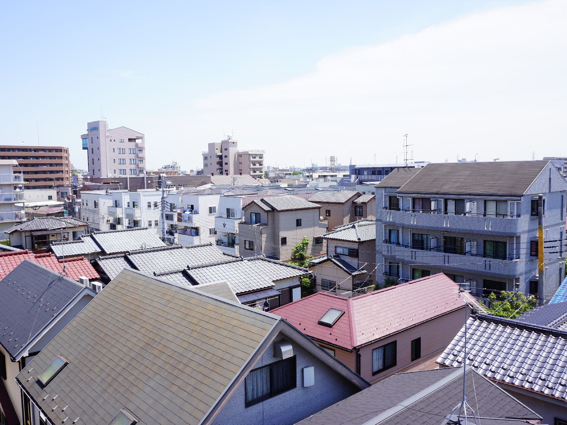 施設の屋上から見える風景である。高層ビルや工場、大きな道路などはなく、住宅が並んでいる。晴れた日の景色である。