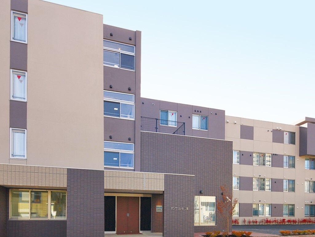 窓がたくさんある。周辺には大きな建物がなく、開放的な雰囲気となっている。建物周囲には植物が植えられている。