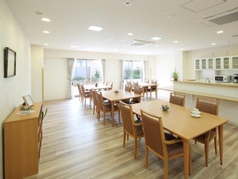 大きな窓から中庭を見ることができるリビングルーム。明るい色のフローリングに、木目調のテーブルと椅子で統一されている。