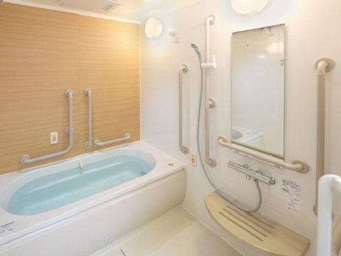鏡やシャワー、浴槽周りに手すりが備え付けられた、木目の壁が特徴的な浴室。一人でも安心して入浴を楽しむことができる。