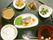 黒く丸い配膳盆に小鉢に盛り付けられた食事が並べられている。焼き魚と白飯やお吸い物などの和食の献立である。