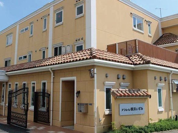 オレンジ色の瓦屋根の３階建ての建物である。低木が植えられた植栽スペースに施設名が表示された看板が立てられている。