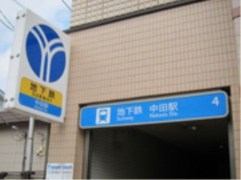 タイルの壁に囲われた入り口、に白文字で地下鉄の駅名が表示された青い看板が設置されている。入り口の前にも地下鉄のマークの看板が立てられている。