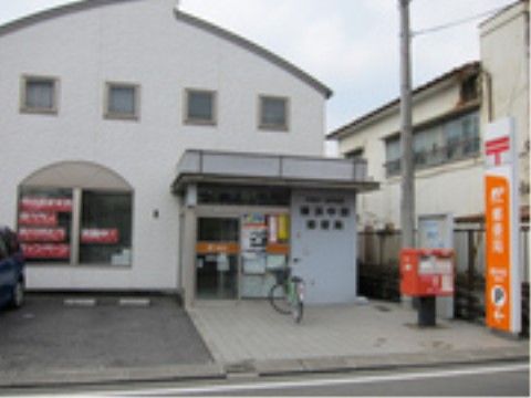 ４つの小窓がついている白い建物がある。自動扉の前はタイルで舗装され、自転車が停められている。看板とポストが立てられている。