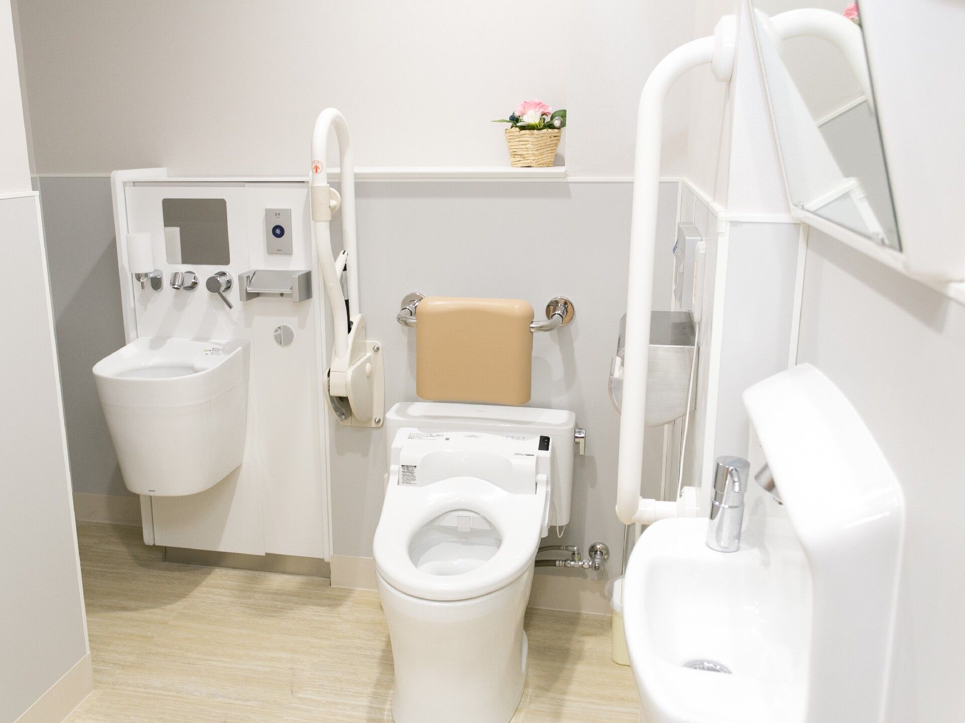 トイレの様子。温水洗浄便座があり、便座の両側に手すりが設置されている。レースカーテンや花が優しい雰囲気を感じさせる。
