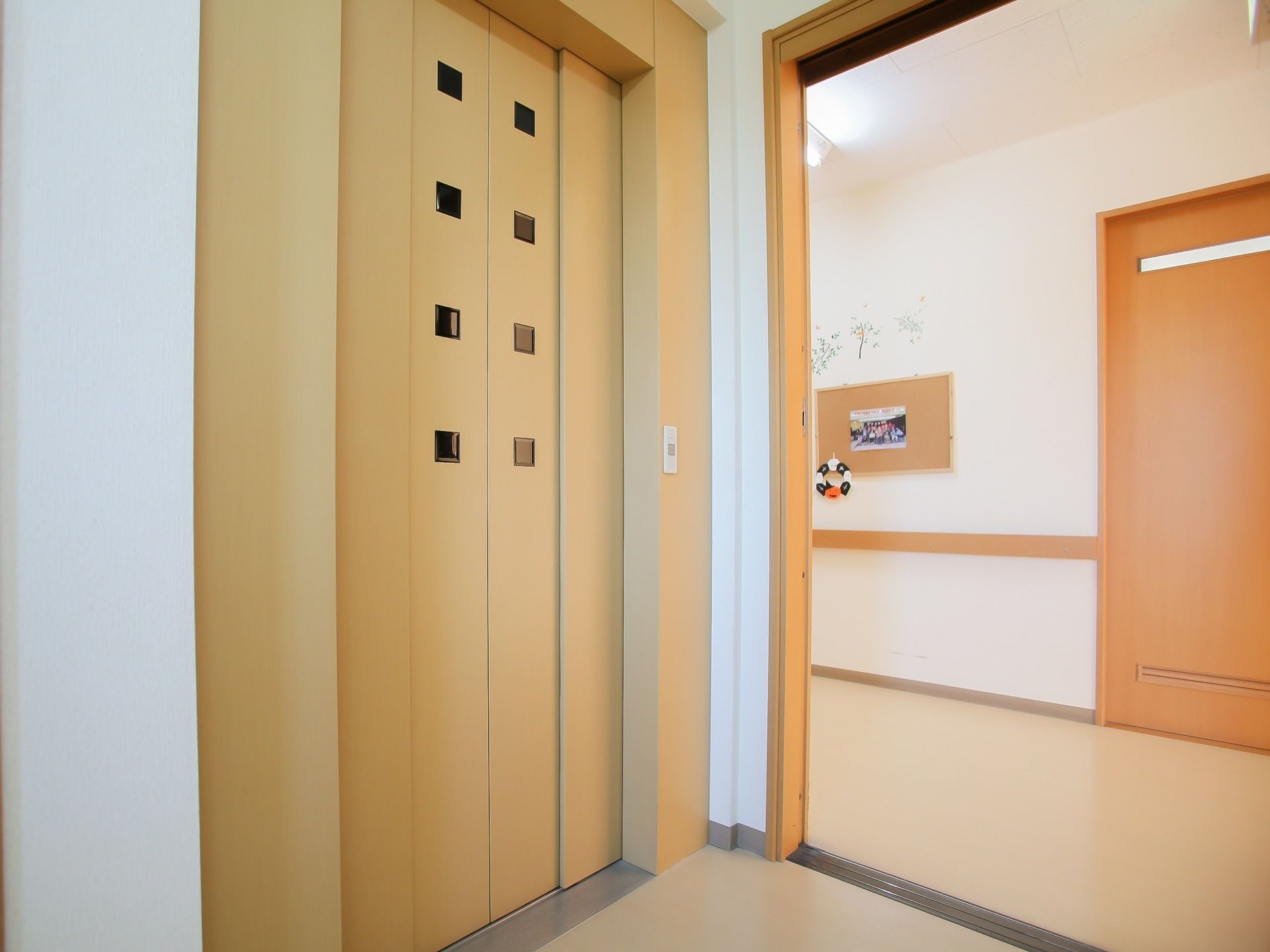 木のぬくもりが感じられるエレベーターである。扉には小さな小窓が設置されており、行先ボタンはシンプルなデザインとなっている。