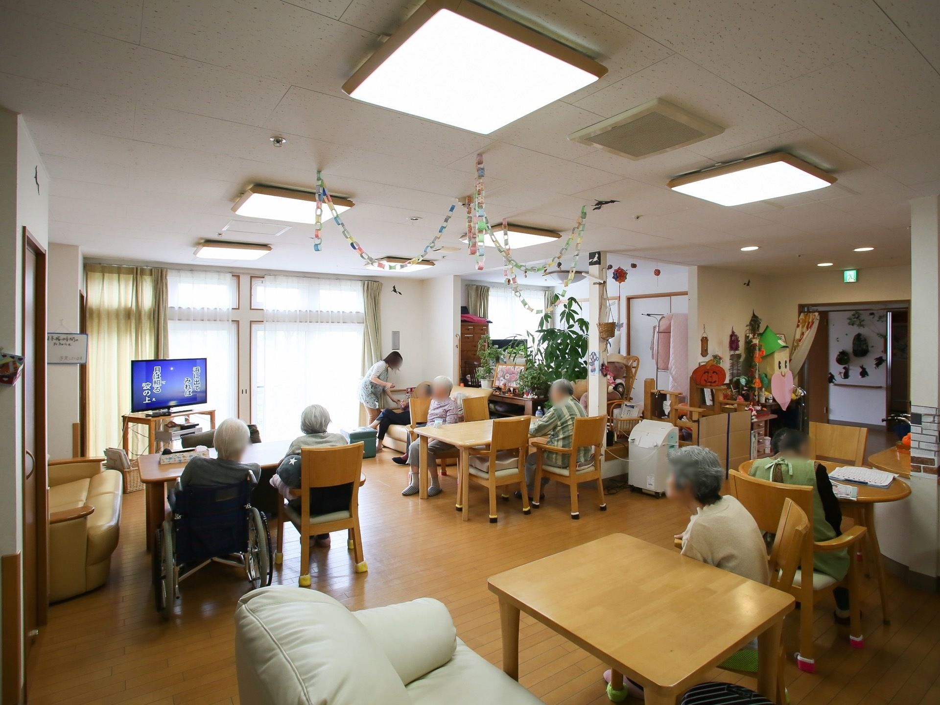 共有スペースの一角には薄型のテレビが設置されている。複数人の入居者様が室内の椅子やソファでくつろいでおり、テレビを観賞している。