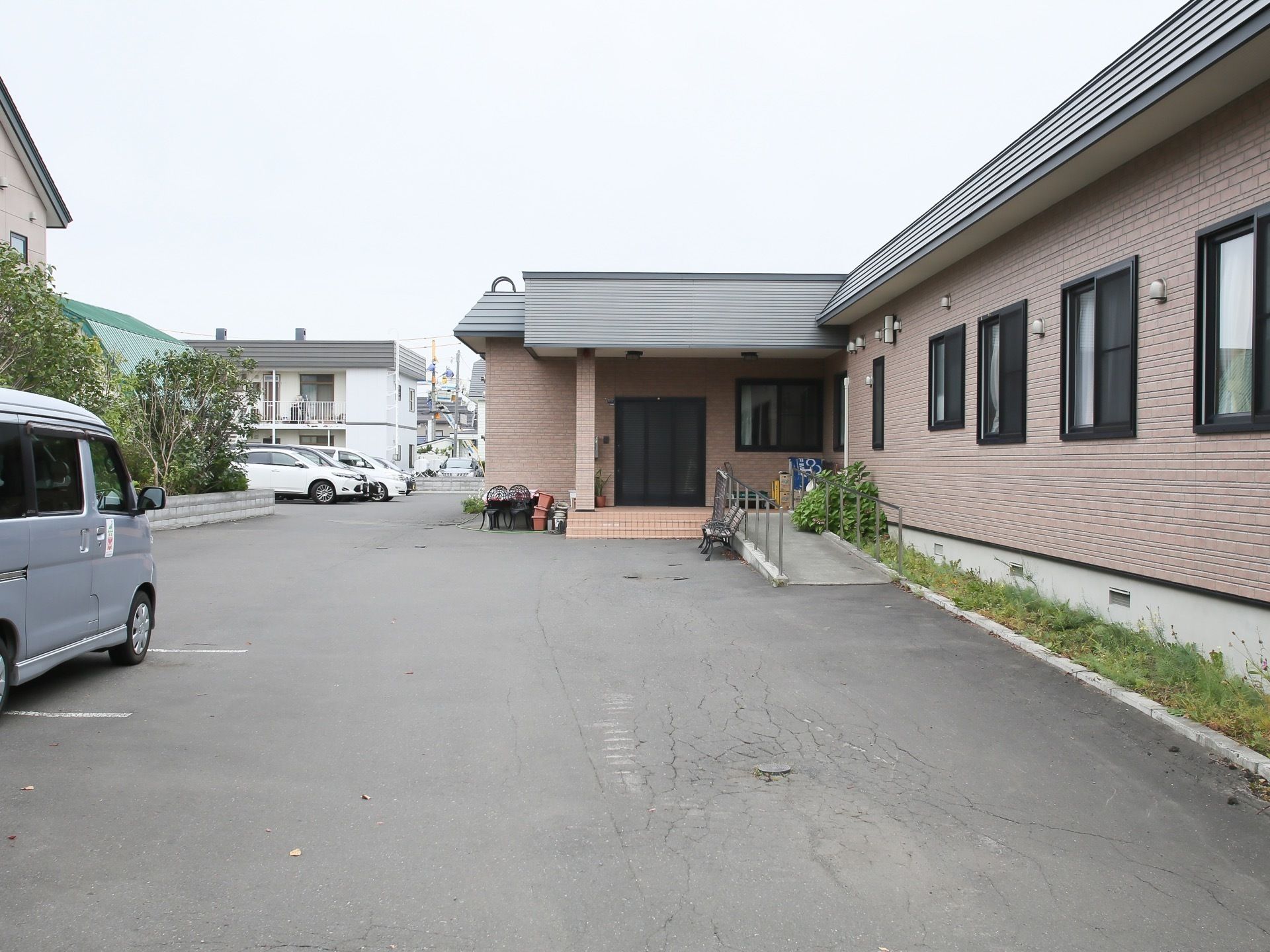 施設の入口周辺には広い空間が確保されており、主に駐車用のスペースとして活用されている。施設は落ち着いた色合いの平屋建ての建物である。