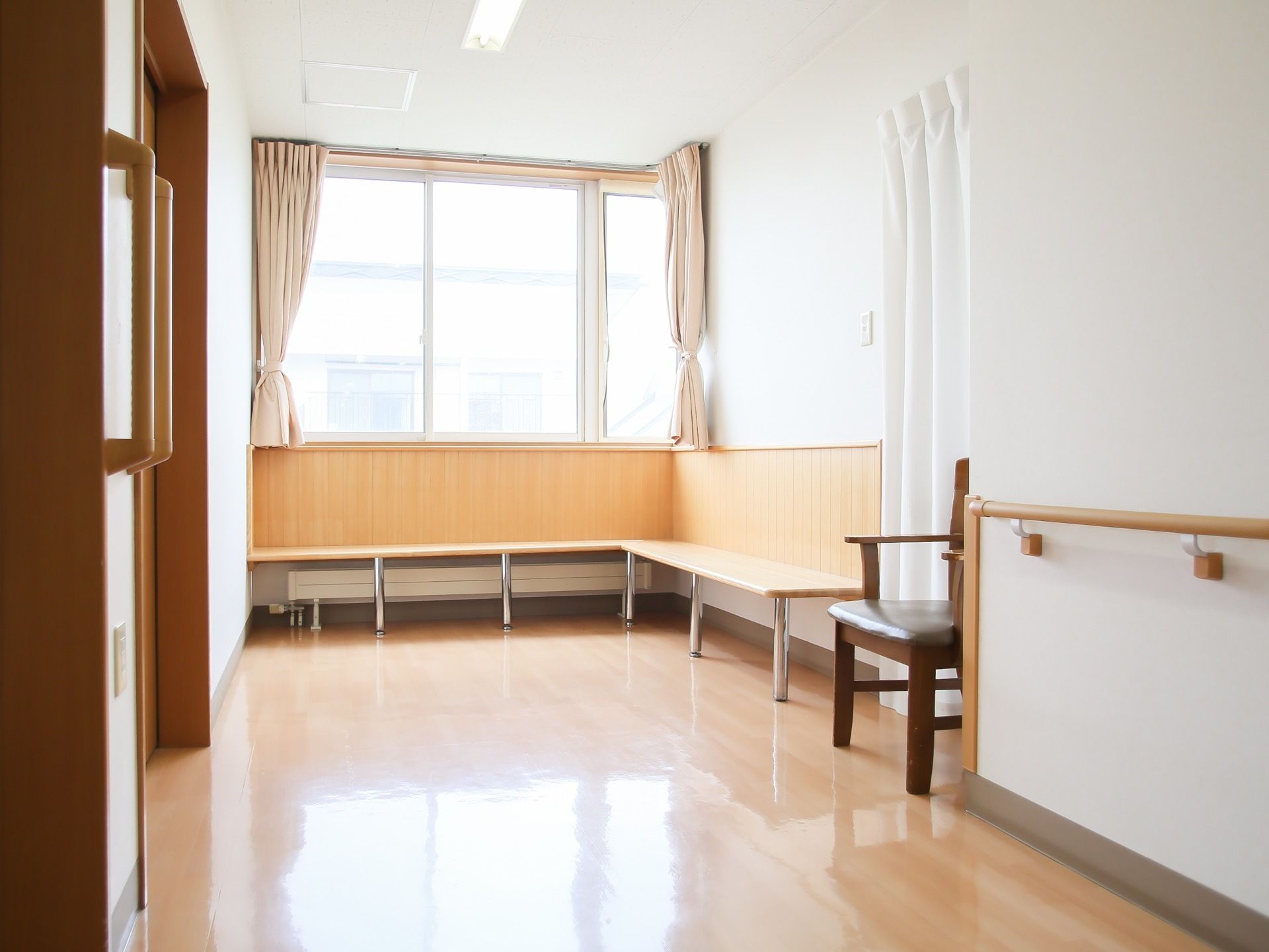 廊下の突き当たりは大きな窓があり、ベージュのカーテンが束ねられている。壁には板材のベンチがL字型に設置されている。