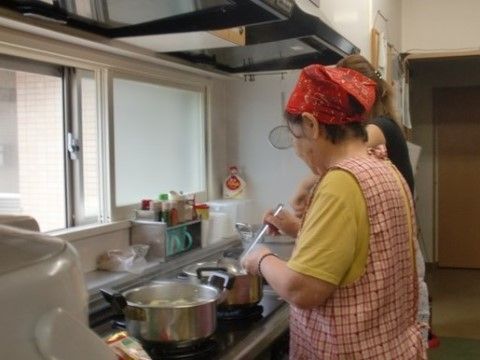 台所で二つの鍋を使って料理をする女性入居者と女性職員