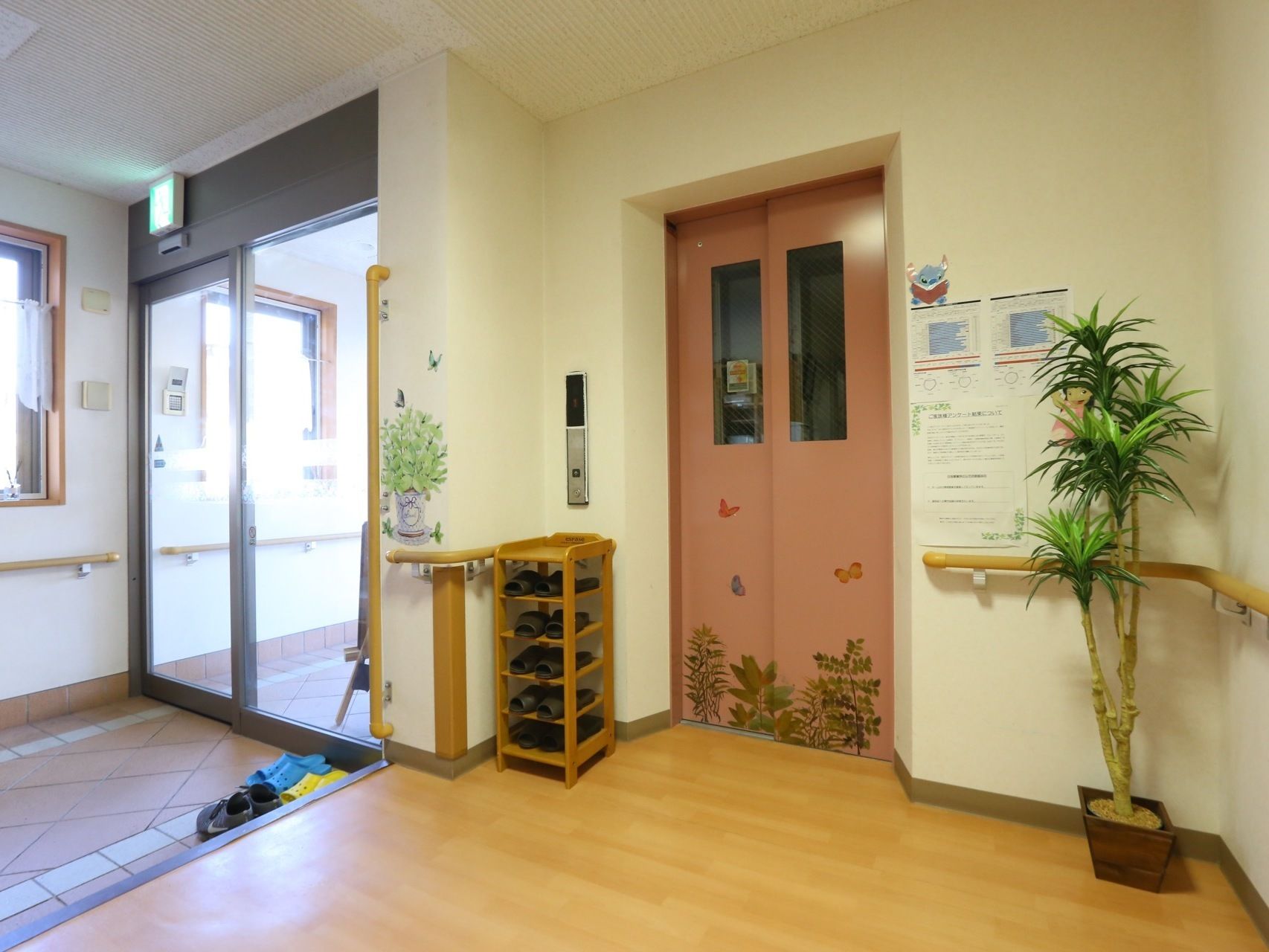 エントランスホールにエレベーターが１基設置されている。ピンク色の扉にはシールでデコレーションされている。