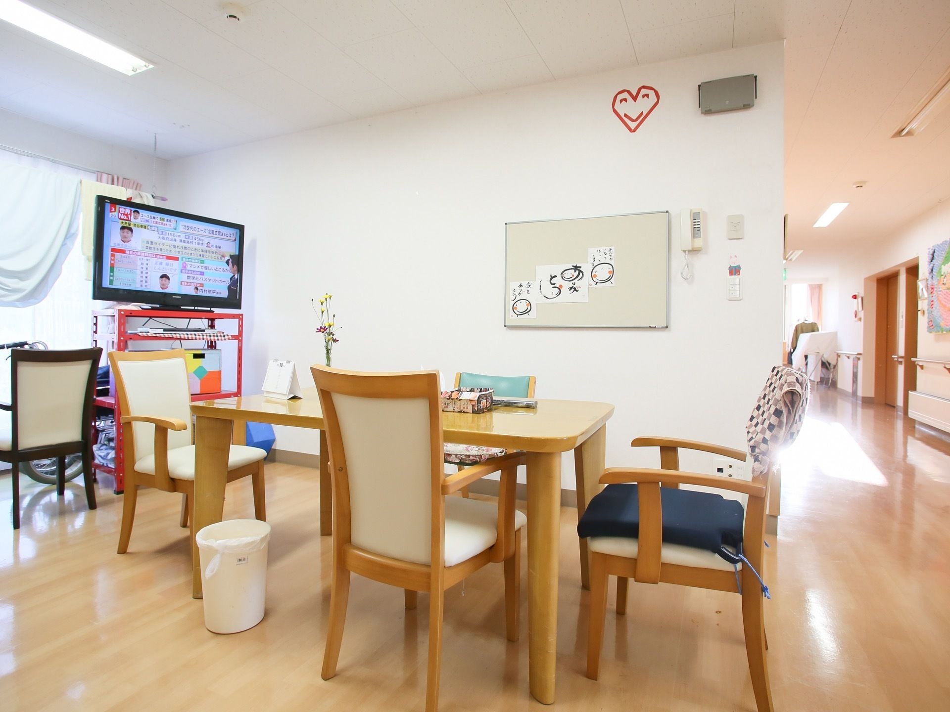 通路途中にある開放的なフロアに、ダイニングテーブルのセットやテレビが置かれている。窓にカーテンが取りつけられている。