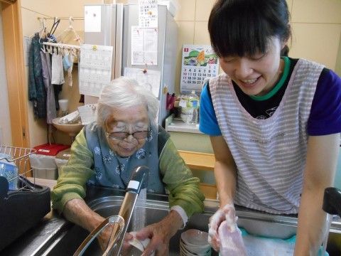 台所で食器を水で流す入居者と洗剤で洗う楽しそうな職員