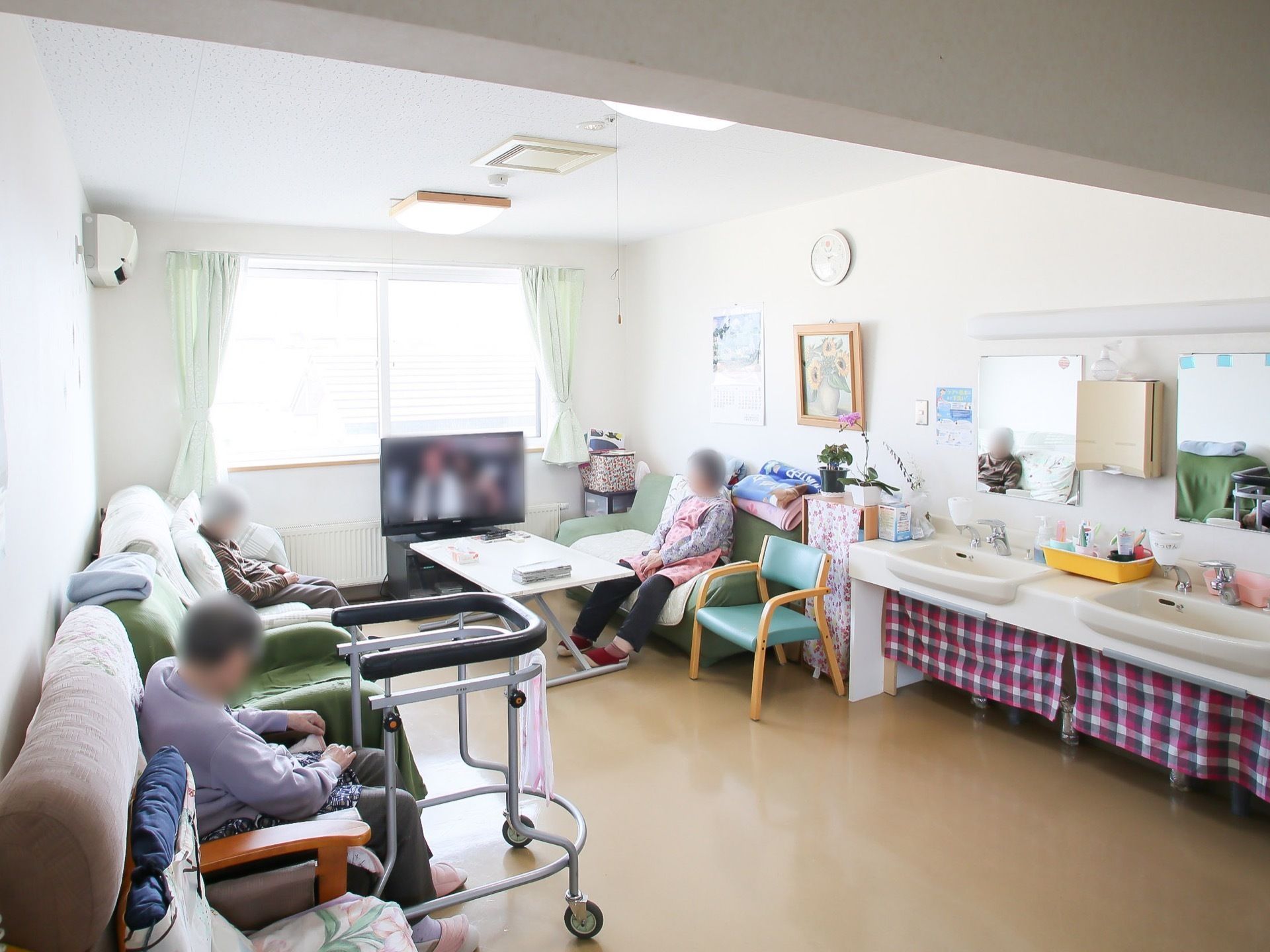 右奥に洗面台が2台つながっている共有スペースの図である。たくさん並べられたソファに入居者様が腰かけている。