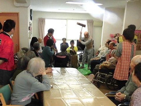 餅つきをする人を座って眺める大勢の入居者と法被を着た職員
