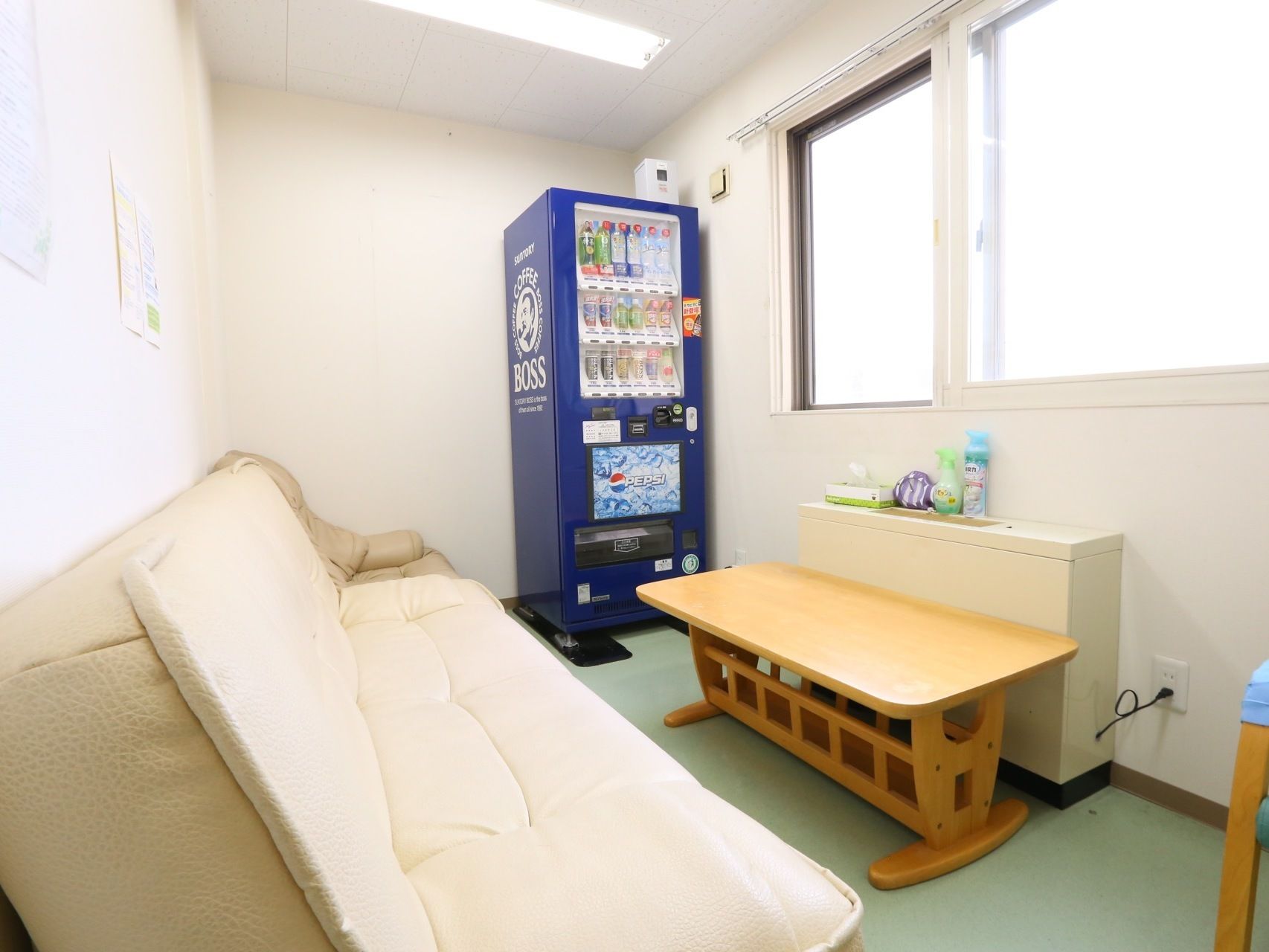 白一色の室内は、明るく清潔感がある。壁際にソファーがあり、前にテーブルと暖房器具が置かれている。部屋の隅には自動販売機が設置されている。
